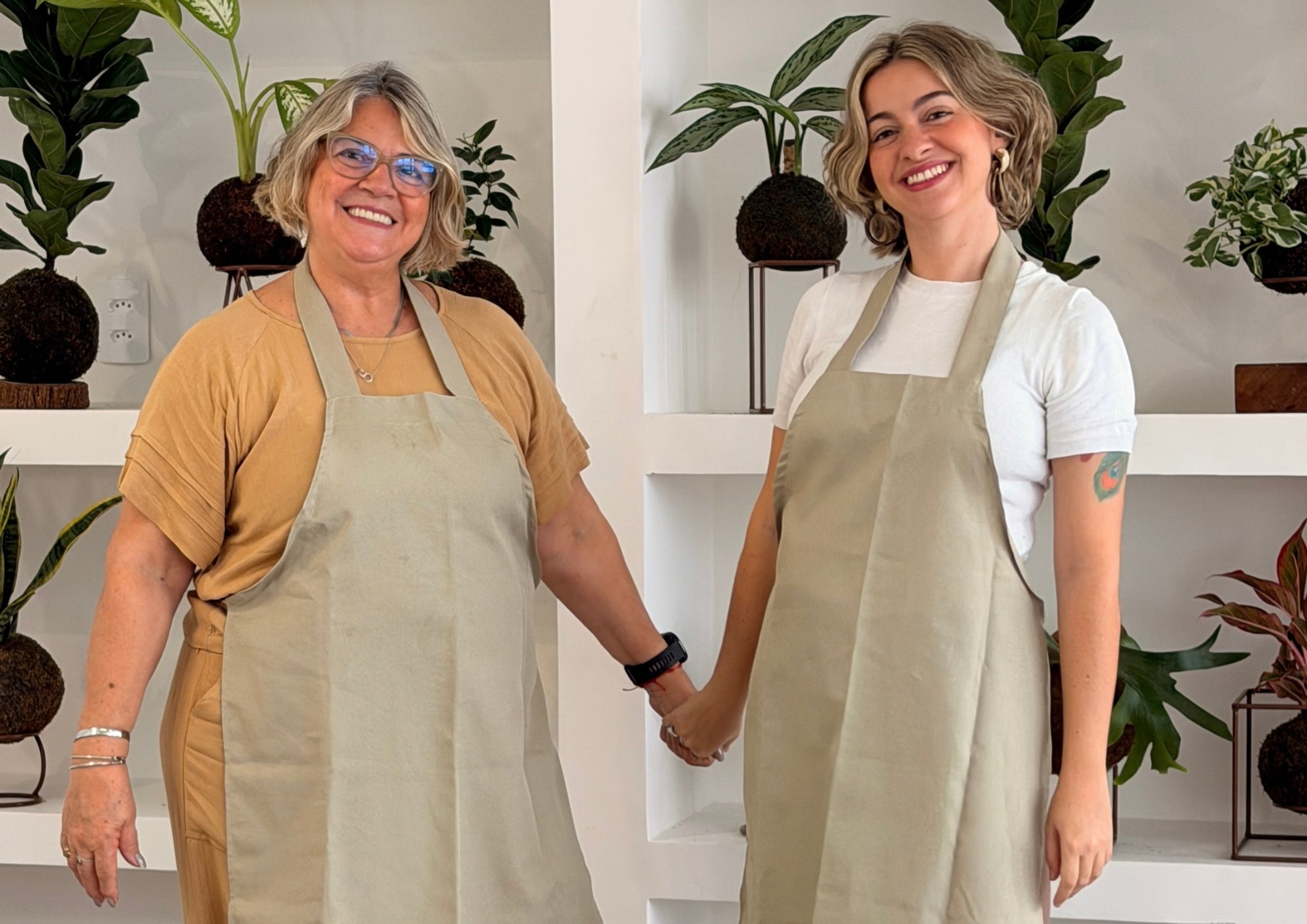 Thaís e Dayse montando kokedamas juntas em uma bancada de madeira